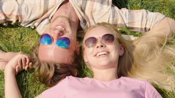 Молодой человек и женщина лежат на траве, смеются, держатся за руки, наслаждаются праздниками — стоковое видео