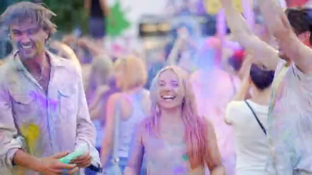 Vrolijke jonge mensen gooien kleurrijke poeder in lucht, dansen op festival — Stockvideo