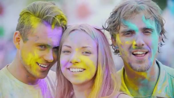 Opgewonden gezichten van prachtige jonge mensen bedekt met kleuren glimlachend op camera — Stockvideo