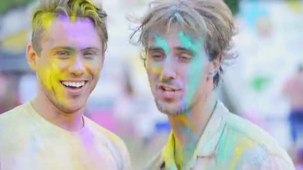 Dois amigos do sexo masculino alegres se divertindo no festival de cores ao ar livre, dando alta cinco — Vídeo de Stock