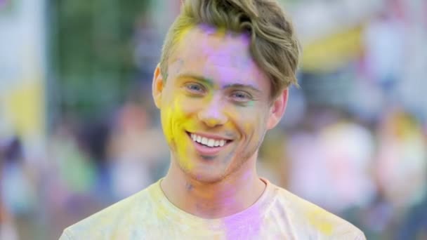 Leende ansikte lycklig ung man skakar huvudet täckt av färgglada färg på festivalen — Stockvideo