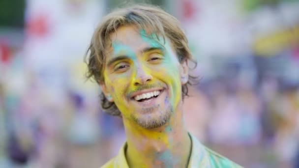 Jovem alegre coberto de corantes coloridos desfrutando de atmosfera no festival — Vídeo de Stock
