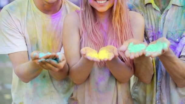 Jeunes gens heureux tenant de la poudre colorée dans les mains, soufflant des colorants à la caméra — Video