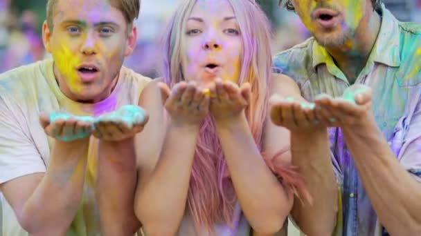 Vrolijke jonge mannen en vrouw waait kleurrijke poeder aan camera op Holi festival — Stockvideo