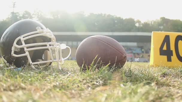 Casco de fútbol americano y pelota acostado en el campo, actividades deportivas campamento de verano — Vídeo de stock