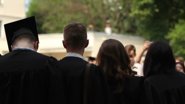 Gelukkige jonge mensen gooien academische hoeden omhoog in de lucht, afstuderen te vieren — Stockvideo