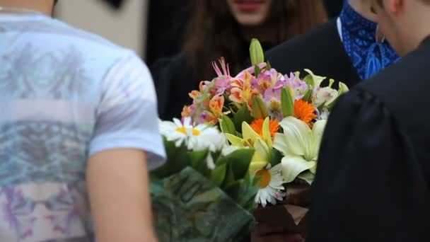 Amigos parabenizando estudantes felizes com a graduação com cachos de flores agradáveis — Vídeo de Stock