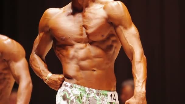 Construtor de corpo bronzeado posando no palco na competição atlética, corpo masculino perfeito — Vídeo de Stock