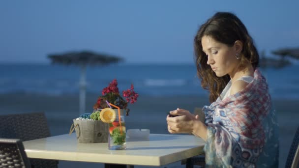 Hermosa señora joven elegante escribiendo mensaje en el teléfono inteligente, relajarse en la cafetería de la playa — Vídeos de Stock
