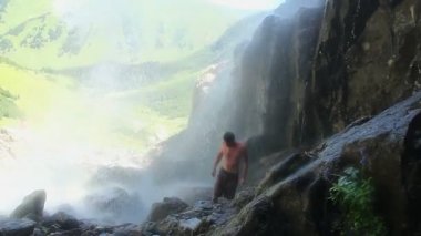 Şelale altında yürüyen gömleksiz adam