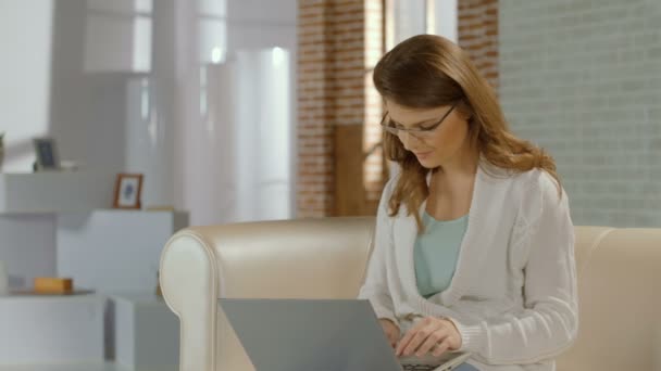 Junge Frau mit Brille, die zu Hause am Laptop arbeitet, schlecht sehend — Stockvideo