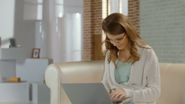 Joven freelancer en gafas escribiendo e-mail, usando laptop — Vídeos de Stock