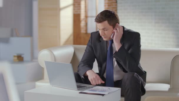 Hombre guapo traje de negocios termina la llamada telefónica, funciona en el ordenador portátil — Vídeos de Stock