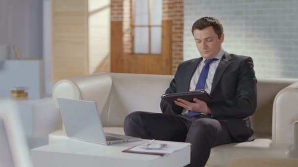 Хорошо одетый бизнесмен ищет прокрутку на планшете в офисе — стоковое видео