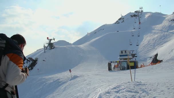 Touriste avec sac à dos regardant la piste de ski enneigée sur les montagnes — Video