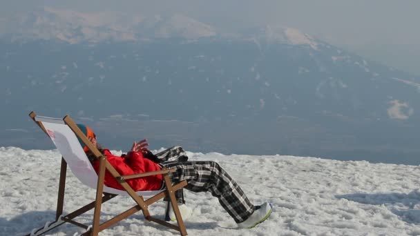 Snowboarder descansando en silla con gadget en la cima de la montaña — Vídeos de Stock