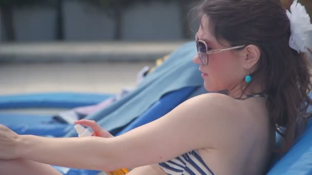 Mooie jonge vrouw in zonnebrillen met zonnebrandcrème op het strand — Stockvideo