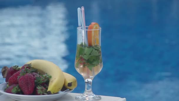 Cocktail en fruit in de buurt van zwembad, blauwe water achtergrond — Stockvideo