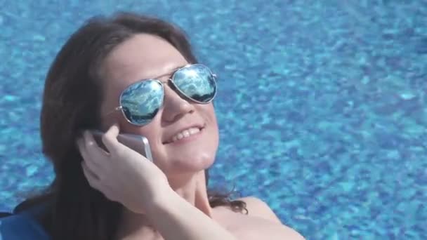 Женщина в хорошем настроении разговаривает по телефону, отражается в солнечных очках — стоковое видео