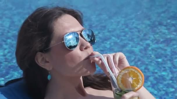 Щаслива жінка п'є холодний коктейль біля басейну, посміхається на обличчі — стокове відео