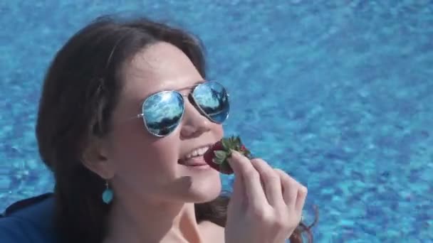 Горячая женщина ест клубнику, улыбается, веселится на вечеринке у бассейна — стоковое видео