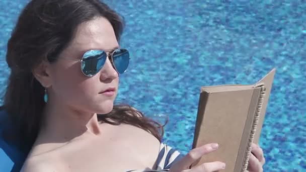 Jovem leitura livro perto da piscina, desfrutando de sol de verão — Vídeo de Stock