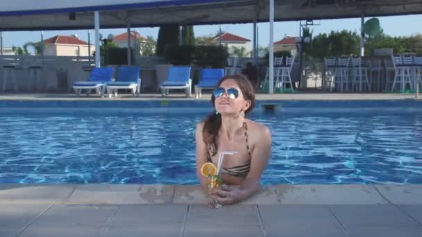 Όμορφη γυναίκα με σέξι σώμα στο μπικίνι πίνοντας κοκτέιλ στην πισίνα — Αρχείο Βίντεο