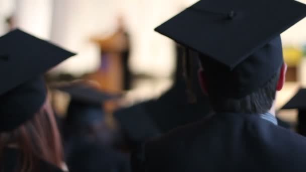 Estudiantes emocionados con gorras y batas aplaudiendo en la ceremonia de graduación universitaria — Vídeo de stock