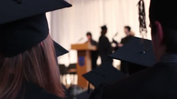 Mujer joven excitada en gorra académica aplaudiendo a graduados. Ceremonia de entrega del diploma — Vídeos de Stock