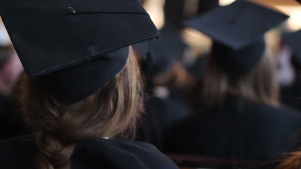 Mujer joven en vestido académico en la ceremonia de entrega de diplomas, escuchando la conferencia — Vídeo de stock