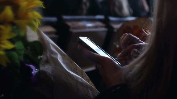 Jovem com cacho de flores usando telefone inteligente no concerto, data romântica — Vídeo de Stock