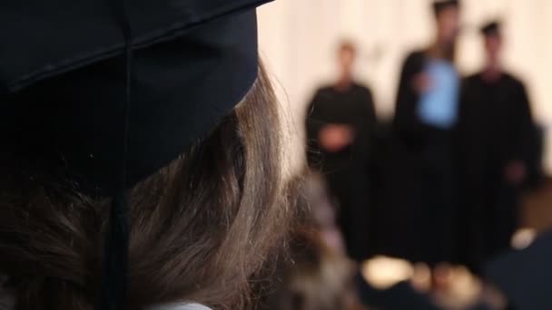 Fille en chapeau académique regardant les étudiants recevant des diplômes, diplôme d'études collégiales — Video
