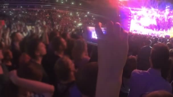 Primer plano de la mano con smartphone filmando concierto de rock en el estadio lleno de gente — Vídeo de stock