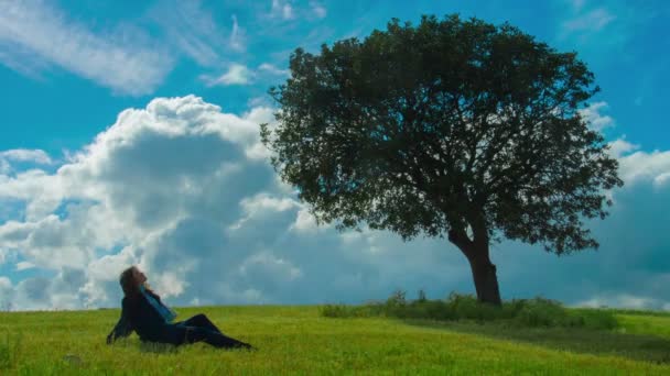 Ensam kvinna sitter under grönskande träd, njuter soliga blåsigt väder, tänkande — Stockvideo