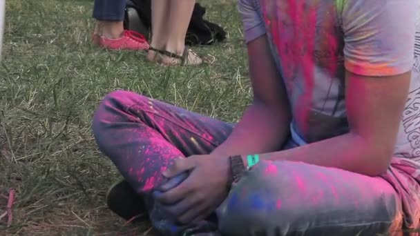 Young man covered with colorful stains sitting on ground, enjoying music fest — Stock Video