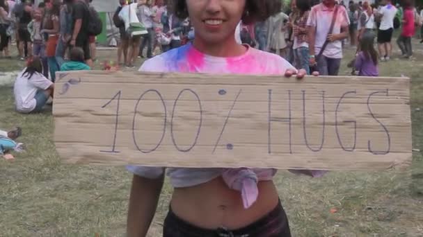 Souriante fille couverte de peinture tenant câlins signe, ambiance de festival, flash mob — Video