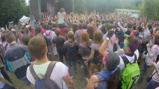 Girl sitting on boyfriend's shoulders spraying colorful powder over happy crowd — Stock Video