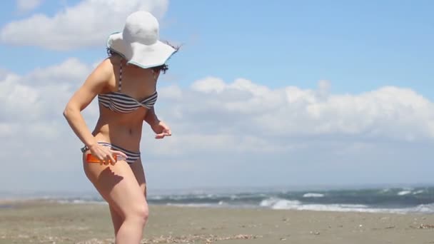 Mujer joven con hermoso cuerpo aplicando aceite solar. Clima ventoso, mar tormentoso — Vídeo de stock