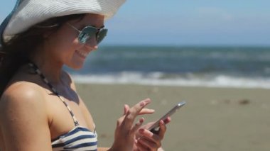Akıllı telefon, fırtınalı deniz, arka planda kumlu plaj da mesajlaşma Oldukça mutlu kadın