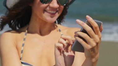 Bikinili mutlu kadın gülümsüyor, yazıyor, mesaj gönderiyor, akıllı telefondan mesaj atıyor