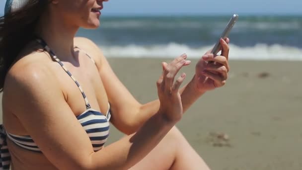 Young woman in bikini making selfie on smartphone, sharing photo on sandy beach — Stock Video