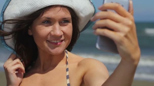 Mujer joven feliz haciendo selfie en la playa junto al mar, tomando fotos en el teléfono inteligente — Vídeo de stock