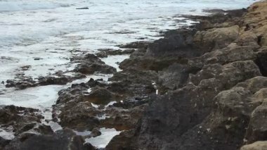 Kayalık deniz kıyısına sıçrayan köpüklü tuz dalgaları, gemi enkazı, soyut döngülü çekim