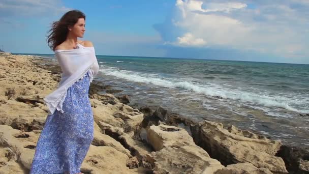 Красивая молодая женщина, завернутая в шарф на скалистом берегу моря, думает о будущем — стоковое видео