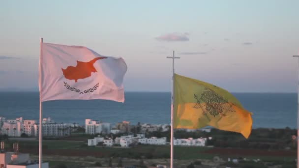 Flaggen Zyperns und der griechisch-orthodoxen Kirche wehen im Wind, im Hintergrund das Meer — Stockvideo