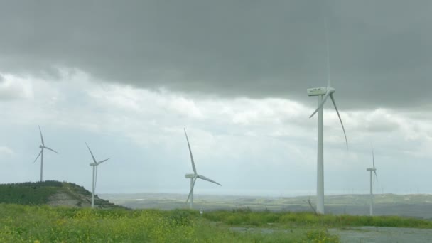 Wind turbines spinning in green field under gray stormy sky, bad rainy weather — Stock Video