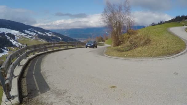 Carro dirigindo na estrada serpentina em montanhas, casas de campo em encostas verdes, paisagem — Vídeo de Stock