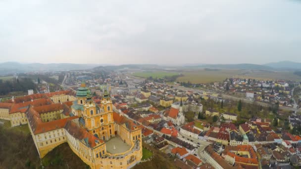 Aerial shot of old European city on river bank, gray sky, mountains on horizon — Stock Video