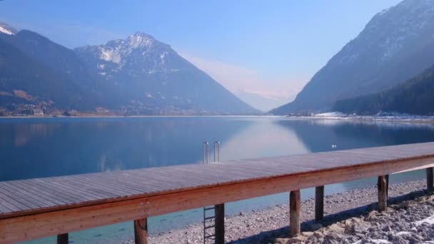 Padella orizzontale del molo di legno vicino al bellissimo lago, montagne coperte di neve — Video Stock