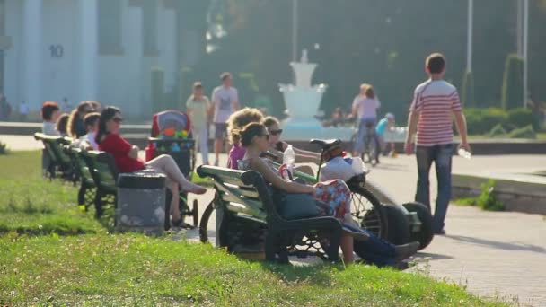 Люди отдыхают на скамейках в парке — стоковое видео